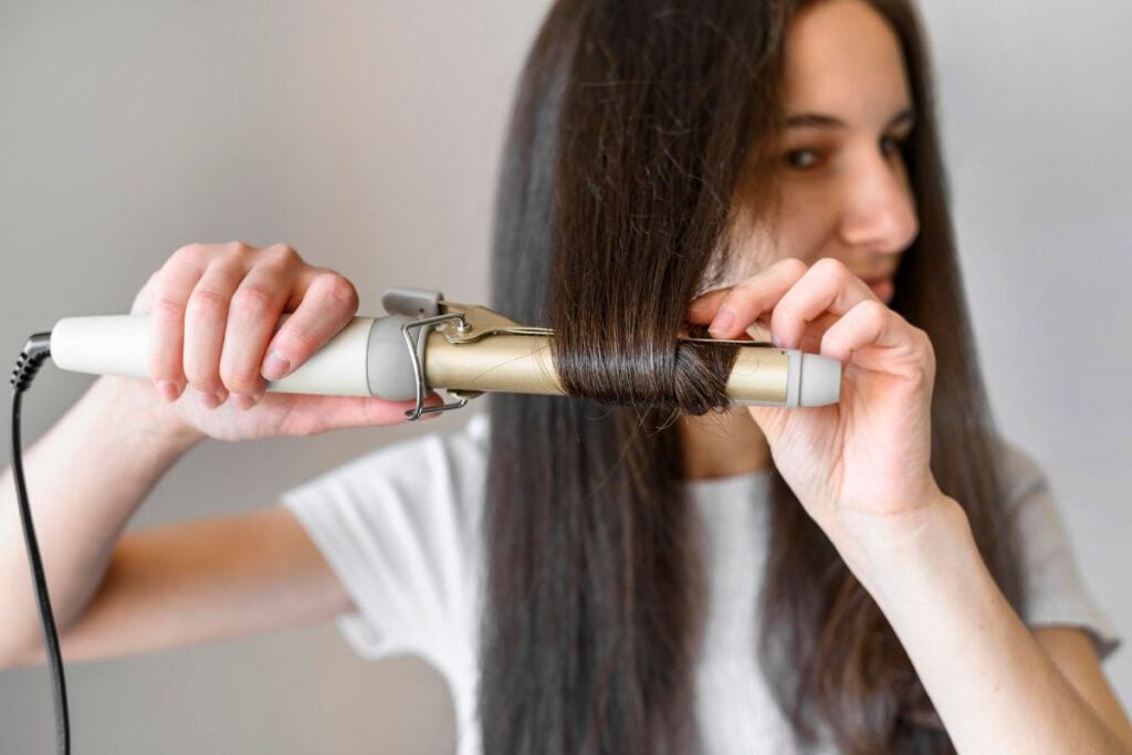 A woman perming her long hair with extensions with a heat styling tool